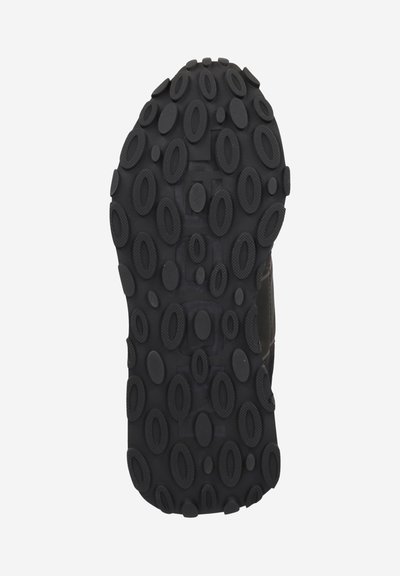 Schwarze Gummisohle mit einer strukturierten Oberfläche, die ovale und kreisförmige Muster für besseren Halt aufweist. Langlebiges Design, geeignet für verschiedene Terrains.
