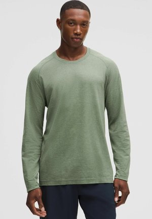 Camicia a maniche lunghe di colore verde tenue con un motivo testurizzato, scollatura rotonda e maniche raglan, realizzata in tessuto morbido e leggero.