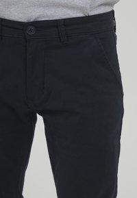 Pantaloni in cotone blu navy con una texture liscia, dotati di chiusura con un solo bottone e tasche laterali, vestibilità aderente e linee pulite.