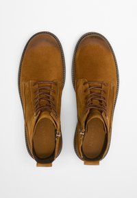 Paire de bottines �à lacets en daim marron avec fermetures éclair latérales, bouts arrondis et semelles cousues sur fond blanc.