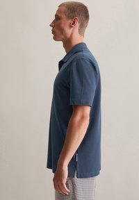 Marineblauwe polo met een klassieke kraag, korte mouwen en zijsplitten voor extra bewegingsvrijheid. Gemaakt van een zacht materiaal.