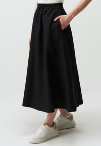 Zwarte rok met elastische tailleband en twee zijzakken, met een vloeiende silhouet en gemaakt van een lichtgewicht stof. Gepaard met witte sneakers.
