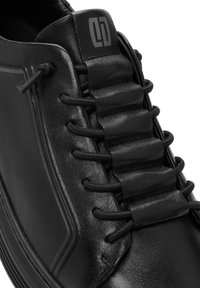 Zwarte sneaker met een gladleren bovenwerk, featuring elastische veters en een subtiel logo op de tong. Ronde neus en een laag profiel zool.