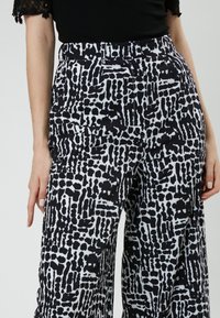 Zwart-witte gestreepte wijde broek met een mix van gedurfde abstracte vormen en lijnen, voorzien van zijzakken en een aangesloten tailleband.