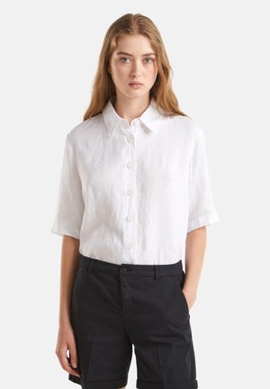 White linen short-sleeve shirt with a collar, featuring button closures and a relaxed fit, paired with black tailored shorts.