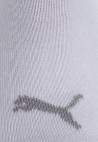 White sock with a small gray Puma logo printed near the ankle on knitted fabric.