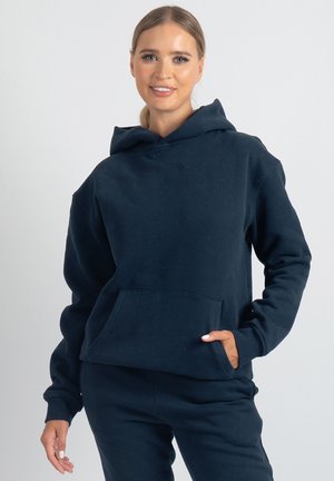 Mornarsko modra jopa iz mehkega blaga z žepom spredaj in kapuco z vrvico. Gladek tekstura z udobnim krojem.