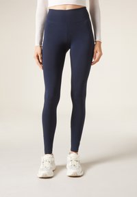 Mörkblå leggings i stretchigt material, med hög midja och en slät textur, i kombination med vita träningsskor.