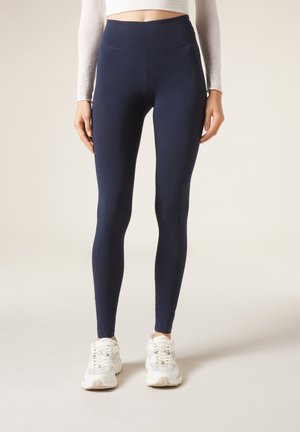 Leggings azul marino hechos de una tela elástica, con una cintura alta y una textura suave, combinados con zapatillas deportivas blancas.