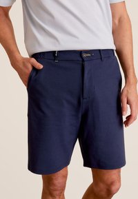 Shorts bleu marine en tissu doux avec une coupe droite, poches avant, ceinture avec un bouton, et une touche de jaune sur la fermeture éclair.