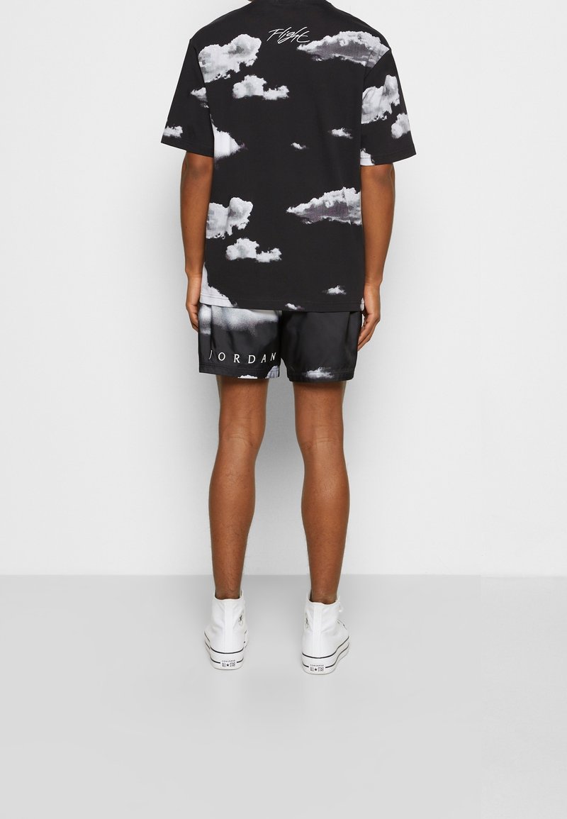 T-shirt noire avec impression de nuages blancs et le texte "Flight", assortie à un short noir arborant un design "JORDAN", le tout complété par des baskets blanches.