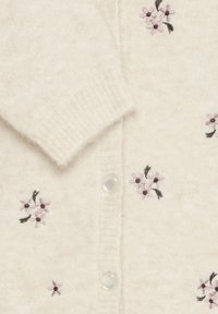 Cardigan lavorato a maglia in crema con una consistenza morbida. Presenta fiori ricamati viola, chiusura con bottoni e polsini a coste.