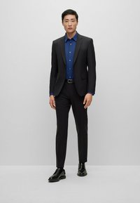 Completo nero con una camicia a fantasia blu. Il design slim-fit presenta rever a scollo, polsini abbottonati e scarpe nere eleganti.