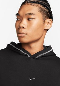 Black hoodie featuring a contrasting gray-lined hood and a small white Nike logo on the chest, made from soft fabric with a smooth texture.