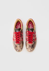 Lacci rossi e strisce su una sneaker con stampa rettile in tonalità beige e marrone. Presenta una soletta imbottita e una suola in gomma.