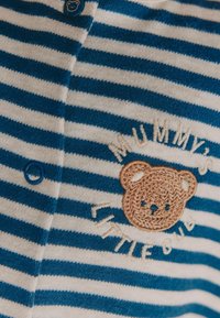 Cardigan per bambino a righe blu e bianche con un bottone blu rotondo, caratterizzato da un orso di peluche ricamato e il testo "Mummy's Little Bub".