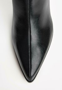 Schwarze Lederstiefelette mit spitzer Zehe, glatter Textur und einer Naht entlang der Seite, vor einem weißen Hintergrund.