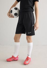 Mustad Nike'i lühikesed püksid valgete aktsentidega, kombineeritud valgete põlvesokkidega ja erkroosade jalgpallikramponidega. Hoidmisel on mustvalge jalgpall.