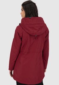 Rode, waterdichte jas met een capuchon, een trekkoord en verstelbare manchetten. Heeft een strak ontwerp en een rugplooi voor gemakkelijk beweegbaarheid.