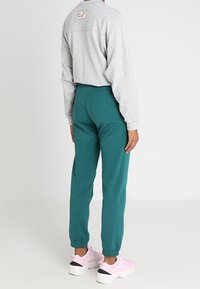 Grå långärmad skjorta med en logotyp-patch, i kombination med teal joggers och rosa sneakers. Har ribbade mudd och en avslappnad passform.