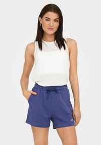 Sportstøj bestående af en hvid ærmeløs top og navyblå shorts med elastisk talje og snørebånd. Minimalistisk logo-detalje på shortsene.