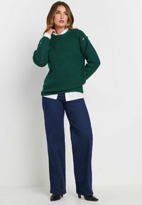 Groene gebreide trui met lange mouwen en een ronde hals, gedragen over een wit overhemd met kraag, gecombineerd met marineblauwe wijde broek.