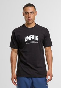 Zwarte katoenen t-shirt met opvallende witte tekst die "ONRECHTVAARDIG" leest en kleinere tekst daaronder: "Ze praten allemaal over cultuur." Eenvoudig ontwerp.