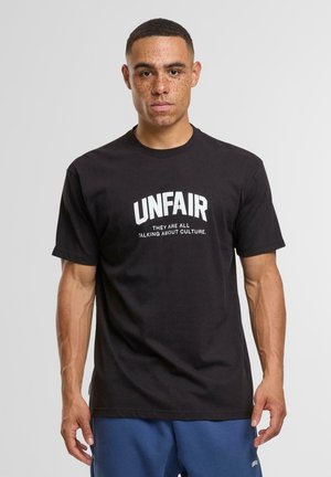 T-shirt in cotone nero con testo bianco audace che recita "UNFAIR" e testo più piccolo sotto: "Stanno tutti parlando di cultura." Design semplice.