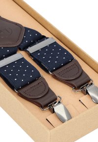 Granatowe szelki z tkaniny z białym wzorem w romby, brązowymi skórzanymi akcentami oraz srebrnymi metalowymi klipsami, prezentowane w kartonowym pudełku.