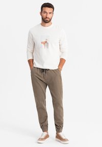 Lichtbeige langarmshirt met een vooropdruk, gecombineerd met olijfgroene joggerbroek met elastische boorden en beige sneakers.