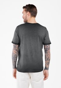 Camiseta de manga corta color gris oscuro con cuello redondo y ribete negro en las mangas. Presenta una textura suave y un corte holgado.