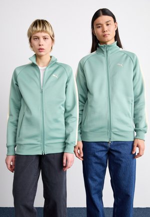 Du modeliai vilki mėtų žalios spalvos zip-up džemperius su raukšlėmis ant rankovių ir kišenėmis, kuriuose yra balta Puma logo ir kontrastingi šoniniai intarpai.