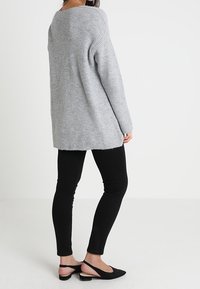 Ljusgrå oversized tröja med ribbad textur, tillsammans med svarta åtsittande byxor och platta svarta skor, sedd bakifrån.