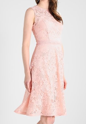 Abito rosa in pizzo senza maniche lungo fino al ginocchio con motivo floreale, vita aderente e scollo rotondo indossato da una donna su sfondo semplice.
