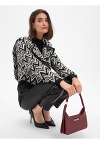 Giacca a motivi bianco e nero con un design cropped, abbinata a eleganti pantaloni neri e una borsa bordeaux con logo.