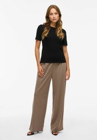 Juodas trumpomis rankovėmis marškinėliai derinami su smėlio spalvos plačiomis kelnėmis. Sklandus, lengvas audinys su laisvu kirpimu ir subtilia tekstūra. Juodi sandalai.