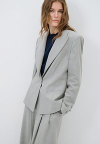 Grijze op maat gemaakte blazer met brede revers, één-knopen sluiting en zachte stof. Gemaakt met bijpassende, losse broek.