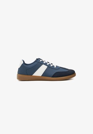 Zapatillas de deporte azul marino con rayas blancas, suela de goma y cordones. Superficies lisas y texturizadas con un diseño atlético clásico.