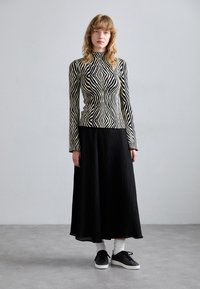 Top de manga larga a rayas blancas y negras con cuello alto, combinado con una falda larga plisada negra y zapatillas negras con suelas blancas.