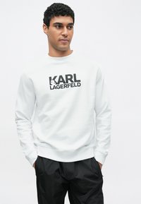 Bílá mikina s dlouhými rukávy, kulatým výstřihem a černým logem "KARL LAGERFELD". Hladká bavlněná látka, pohodlný střih a žebrované manžety.