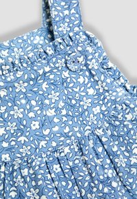 Mono de tela azul con patrones florales blancos, tirantes elásticos fruncidos y detalles plisados, hecho de material suave y texturizado.