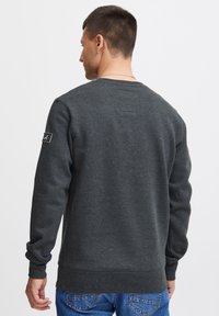 Donkergrijze sweatshirt met lange mouwen, ronde hals, en geribbelde manchetten en zoom. Heeft een klein logopatch op de linker mouw.