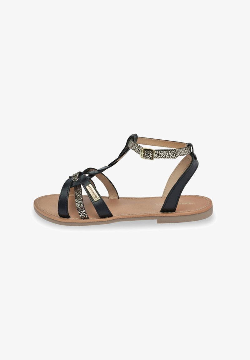 Sort strappy sandal med glat læder og metallic-detaljerede stropper, der har en spænde-lukning og en flad, tan-farvet sål.