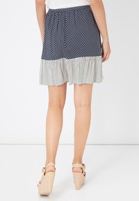 Mujer que lleva una falda azul marino con lunares blancos y un dobladillo de volantes a rayas blancas, combinada con sandalias de cuña beige, de pie.