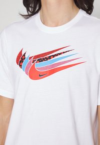 White cotton t-shirt with a colorful Nike logo featuring red, blue, and black patterns resembling swooshes across the chest.