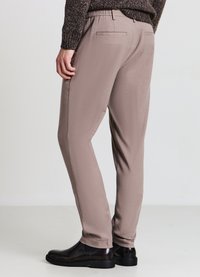 Hellbraune Stretchstoffhosen mit schmaler Passform, elastischem Bund und zwei Gesäßtaschen, kombiniert mit schwarzen Lederschuhen.