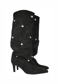 Botas altas de ante negras que presentan una punta afilada y un tacón de aguja. Decoradas con remaches en tono plateado a lo largo del caña para aportar detalle.
