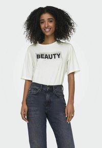 Witte T-shirt met korte mouwen, voorzien van zwarte "BEAUTY" tekst en rhinestone accenten, gecombineerd met high-waisted donkere spijkerbroek.