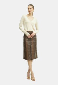 Top beige a maniche lunghe con scollo a V abbinato a una gonna a tubino in faux serpente marrone, dotata di una vita e di uno spacco frontale.