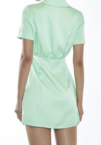 Robe vert menthe en satin avec un col à revers, des manches courtes et une taille élastique, présentant une coupe courte et ajustée avec des détails minimalistes.